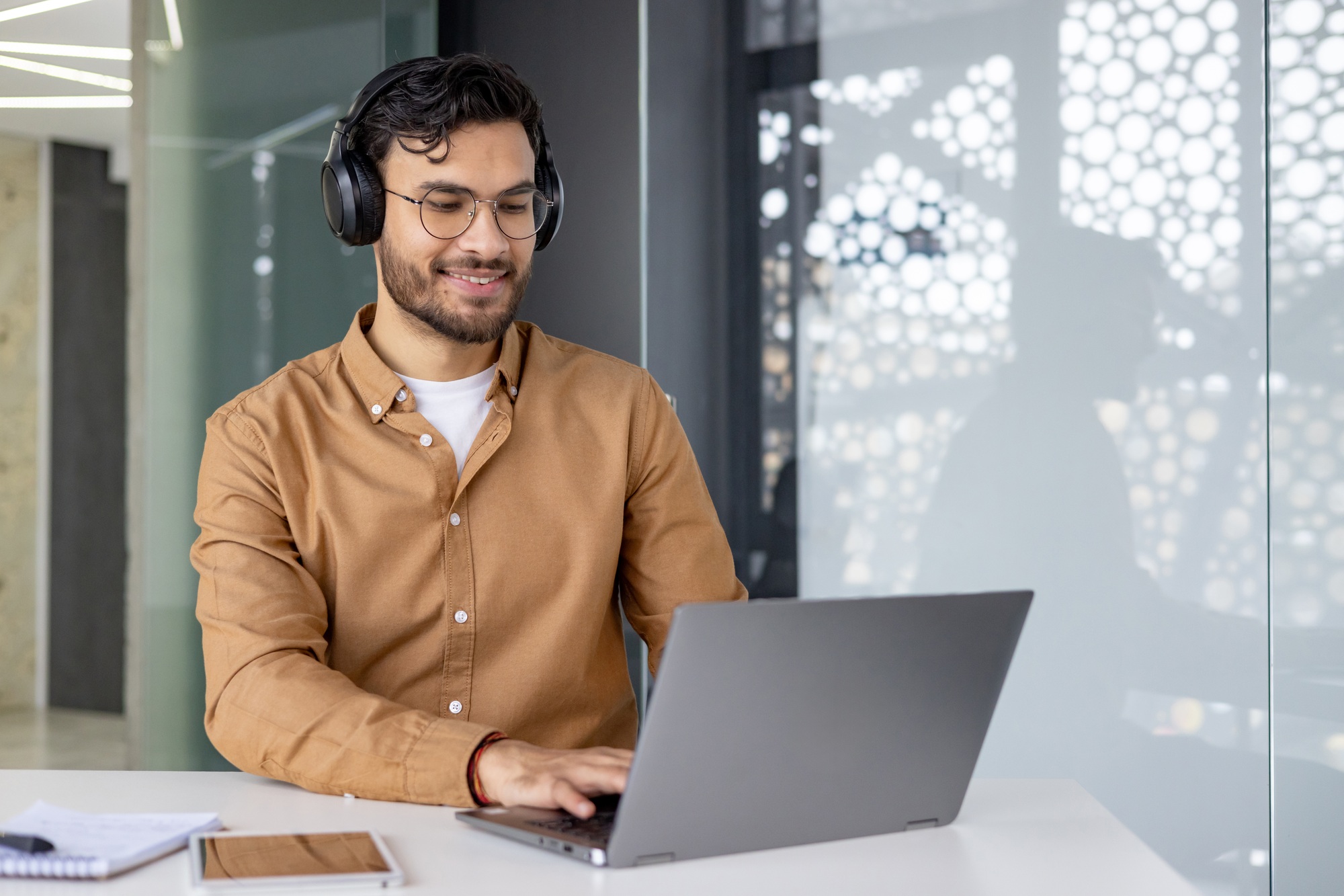 Smiling man with headphones working on a laptop in a modern office